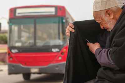 Elderly Man Checking His Phone Beside a City Bus