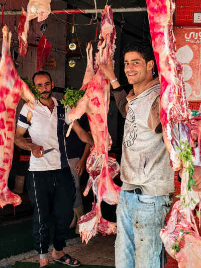 Butchers Laughing Beside Hanging Meat in a Traditional Market