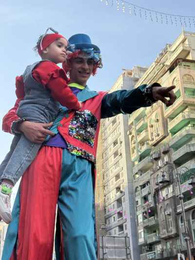 Clown on Stilts Carrying a Baby Girl on Eid Morning in Alexandria