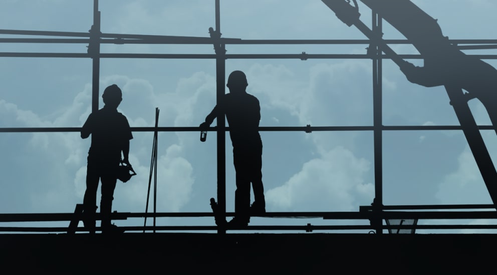 Two construction workers standing on scaffolding. 