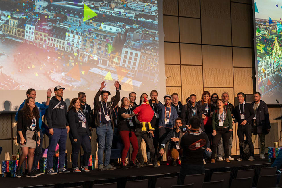 Group of people at DrupalCon Prague 2022 holding a red chicken in front of a screen