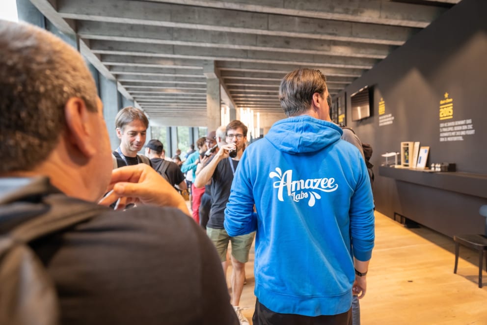 Attendees having a drink, back of one attendee wearing blue hoodie with Amazee Labs branding