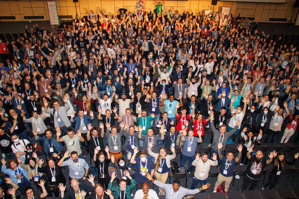 Large group of people looking upwards towards the camera with their arms in the air