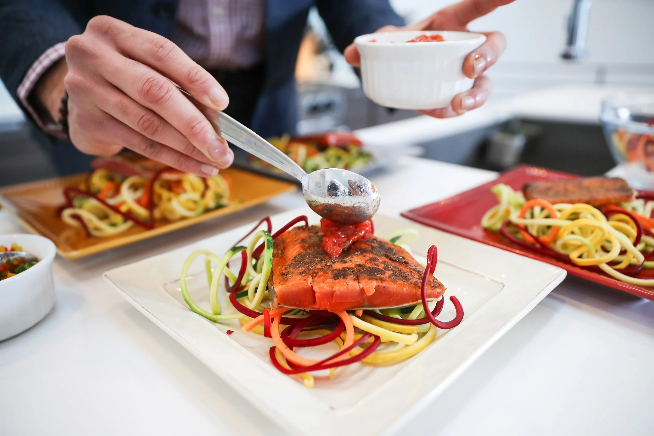 Chef plating a fish dish with spiral vegetable noodles
