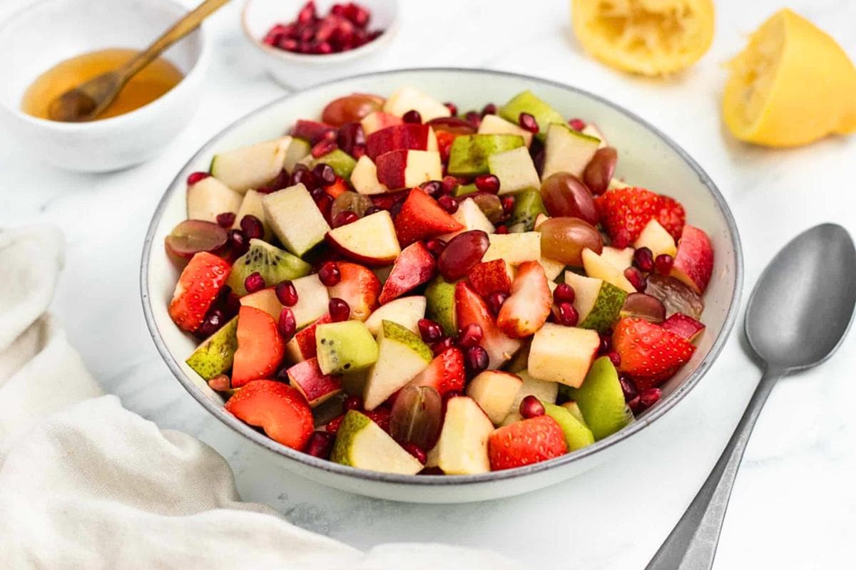 A fruit salad with colorful melon, grapes, and berries in a clear bowl.
