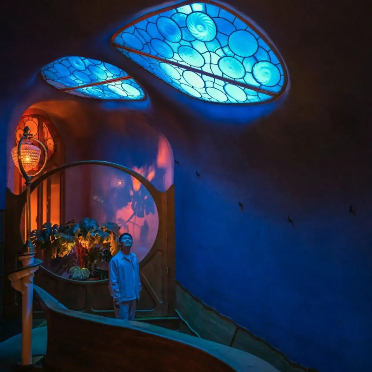 Una persona si trova in una stanza con architettura organica, finestre del soffitto illuminate di blu e illuminazione decorativa calda.