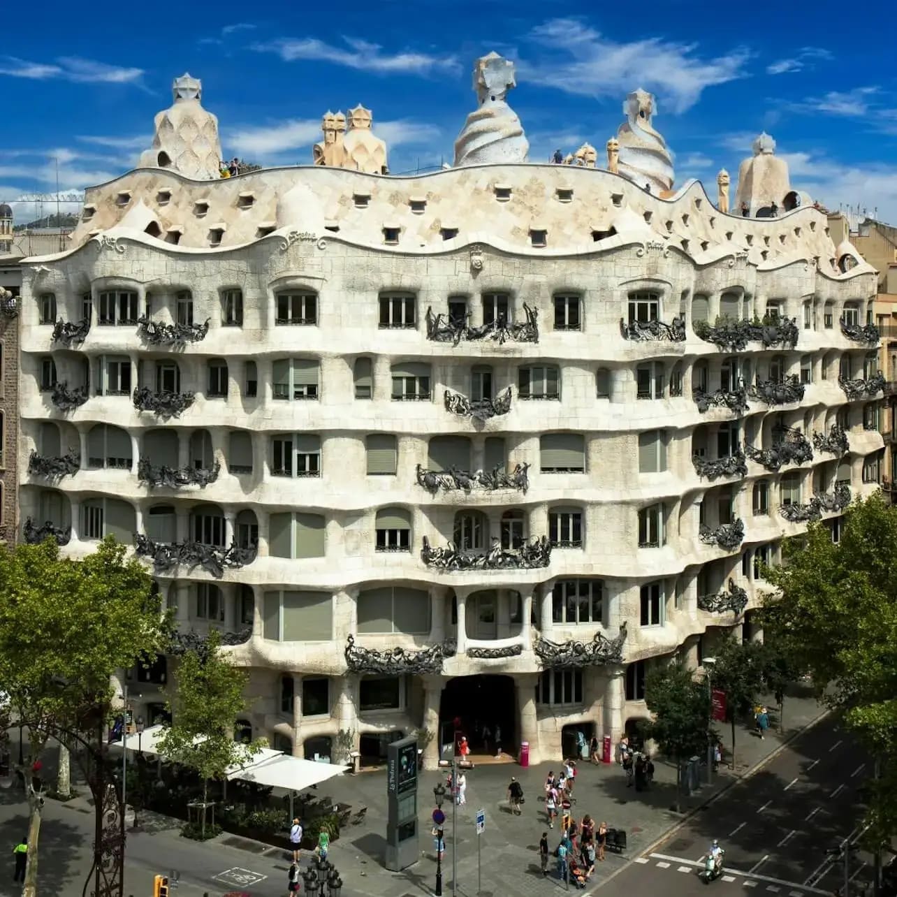 Un gran edifici ornamentat amb parets ondulades, nombroses finestres i xemeneies corbes úniques a la teulada, sota un cel blau.