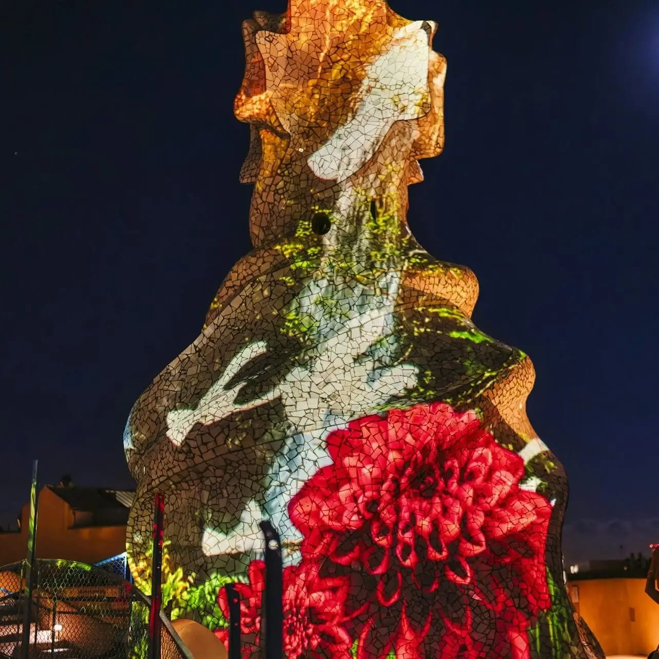A tall, irregularly shaped structure with projected images of birds and a large red flower against a dark night sky.