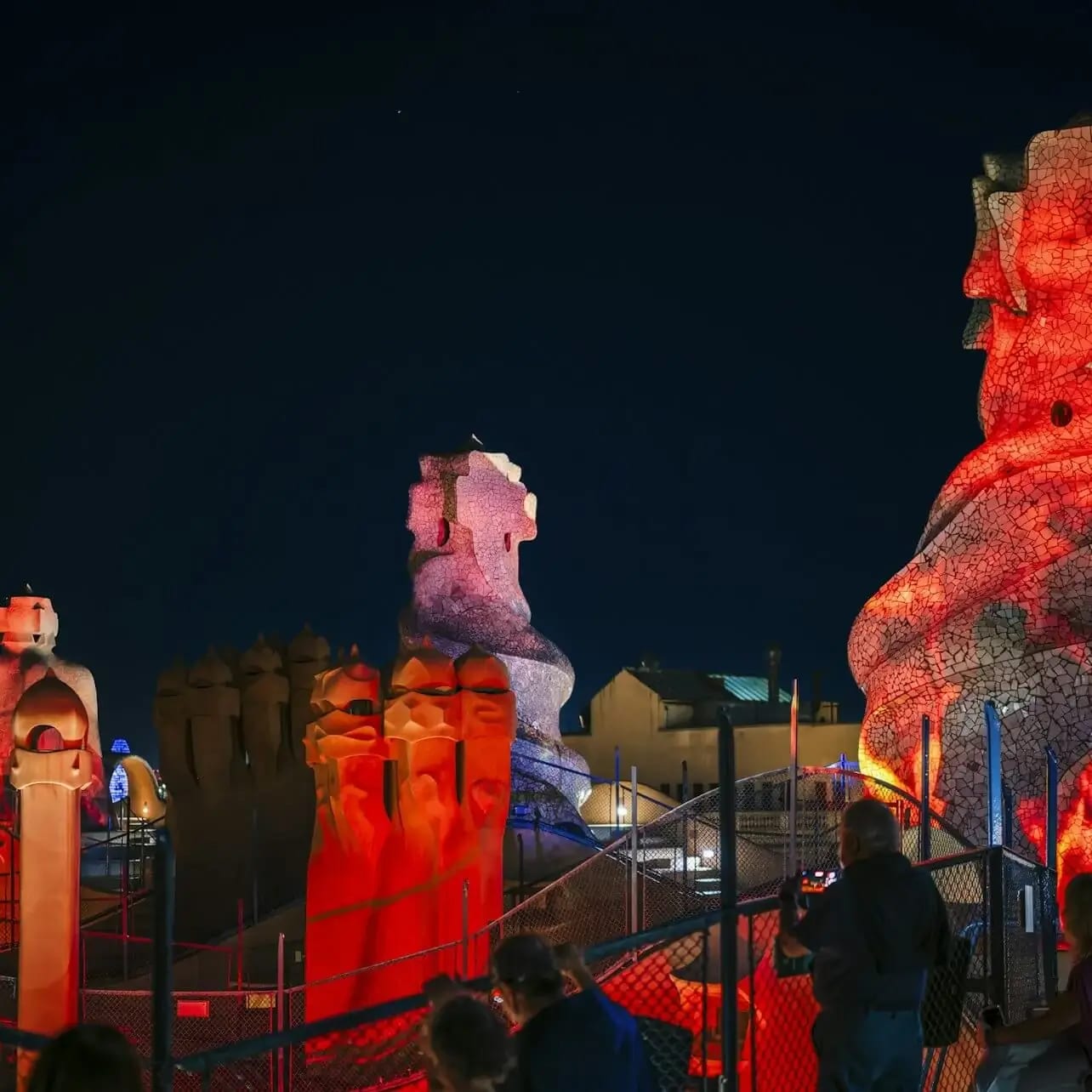 Turistes en un terrat de nit admiren escultures de pedra abstractes, acolorides i il·luminades en un famós lloc arquitectònic.