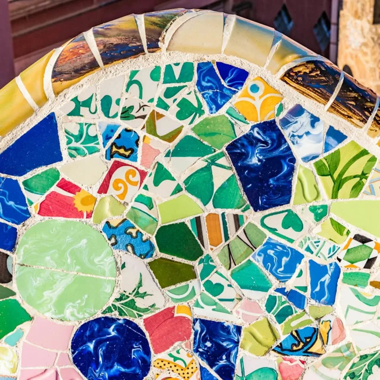 Primer pla d’un mosaic colorit amb formes i patrons variats, en tons blaus i verds vibrants, amb un edifici de fons.