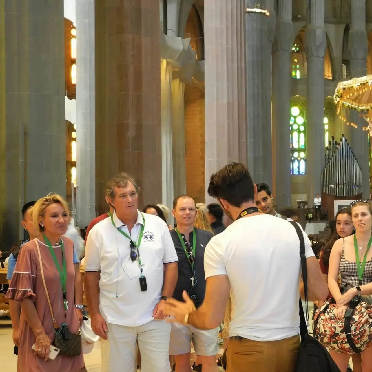 Guia turístic explicant l'interior de la Sagrada Família a un petit grup de visitants entre altes columnes de pedra i vitralls acolorits.
