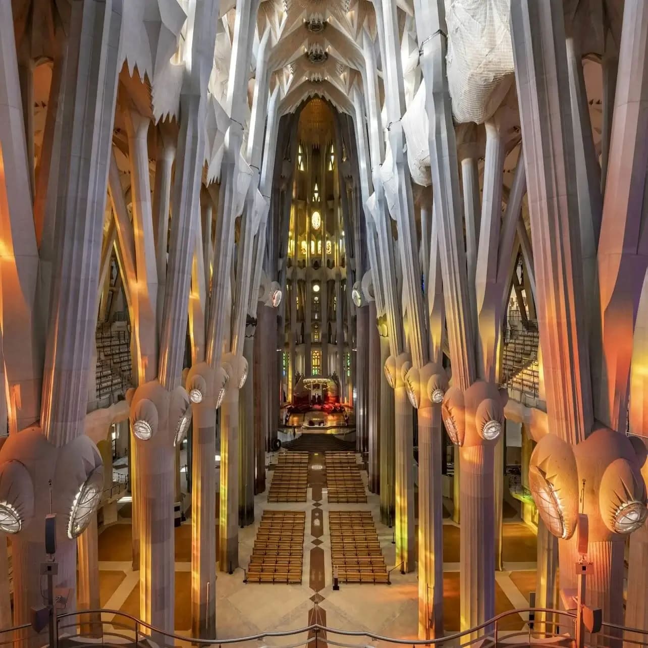 Interior of a grand cathedral with high, ornate columns, vibrant stained glass lighting, and symmetrical seating arrangements.