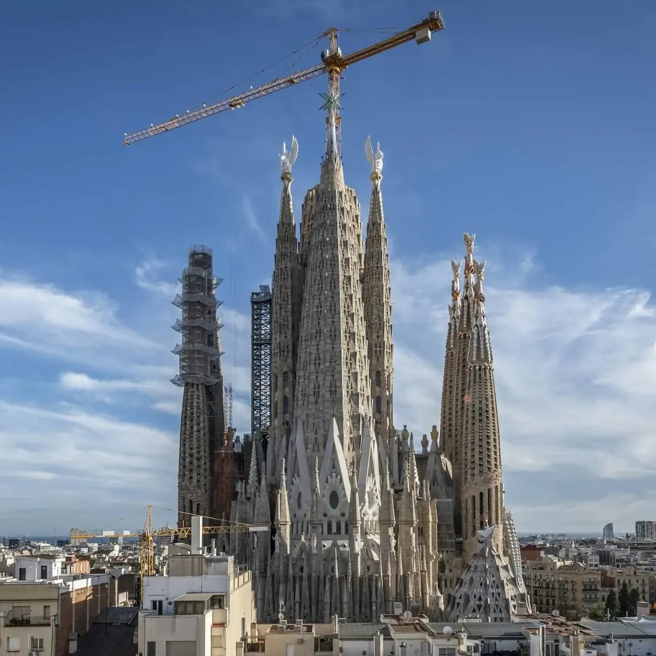 Una gran basílica en construcció amb diverses torres altes i una grua a la part superior, sota un cel blau clar.