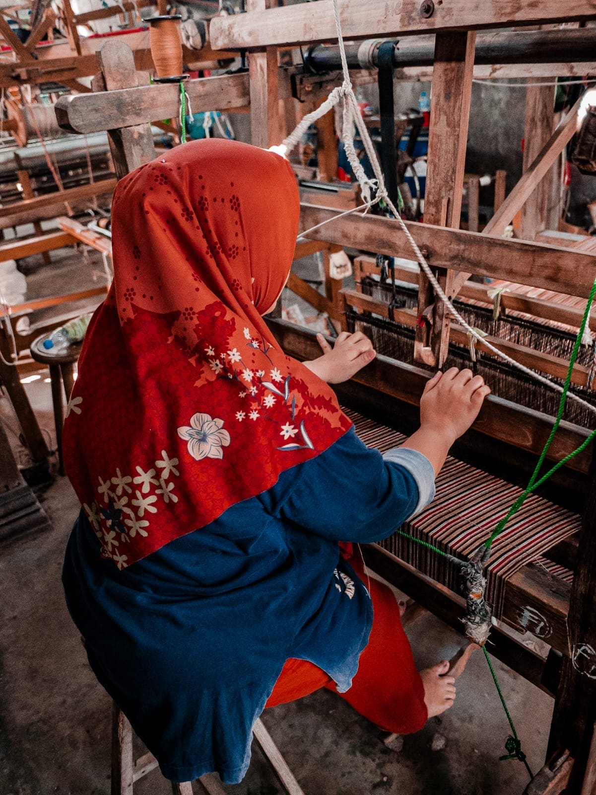 Traditional Indonesian weaver working on handloom with colorful striped fabric in Yogyakarta