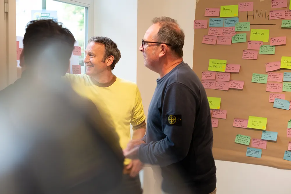 Das Foto zeigt drei Workshop-Teilnehmer vor einer Fensterscheibe mit Post-its.