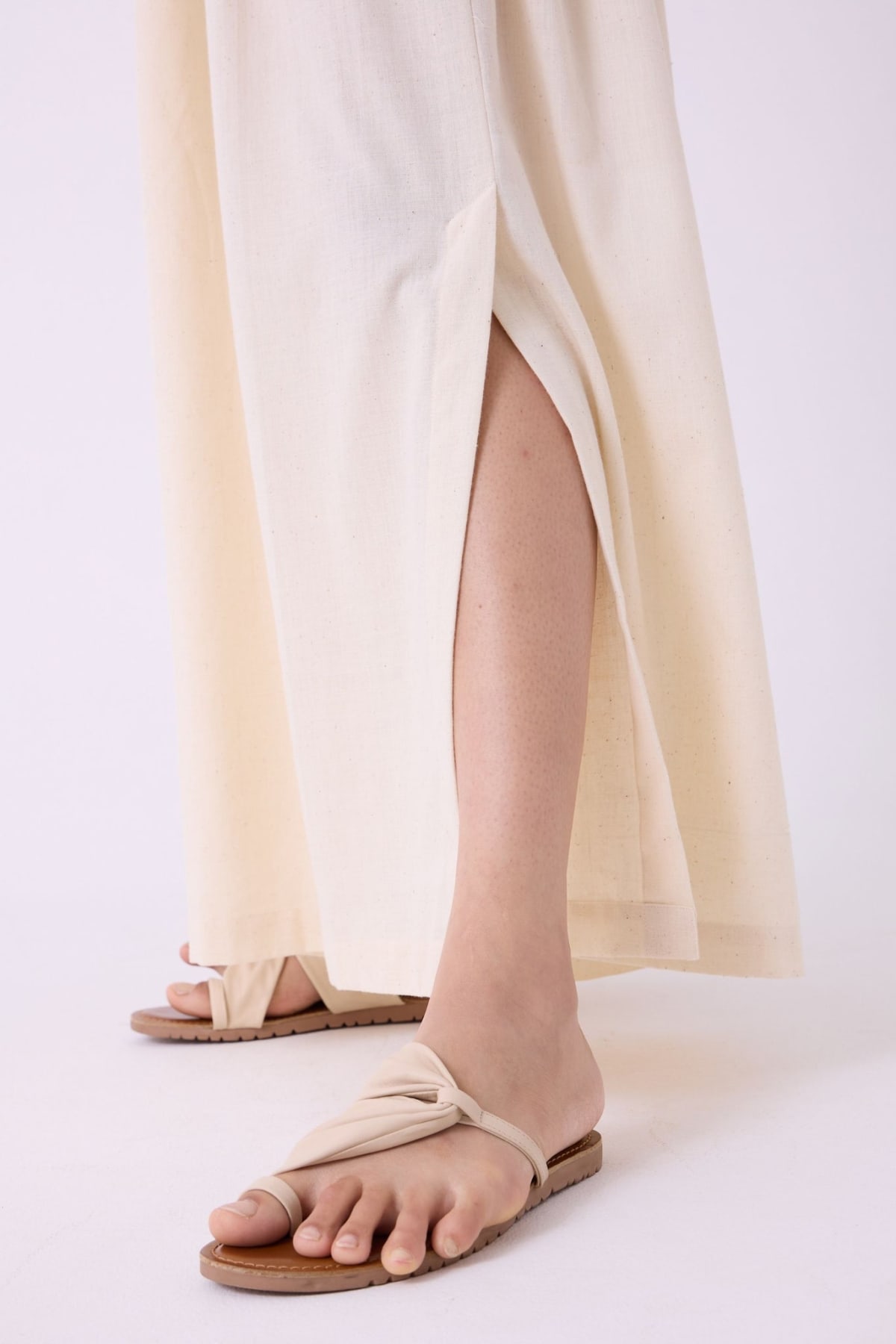Official product photograph of the Takumi trousers' lower leg: the side opening parts over the calf above the hem, with a sandal, on a white studio background.