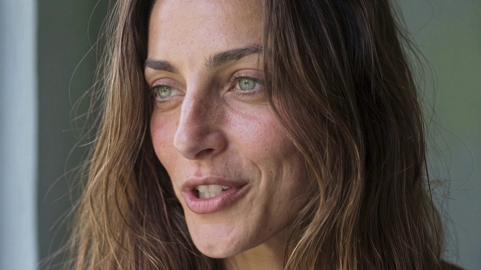 Close portrait of the woman, hair loose around her face, lips parted in a small smile as she looks off to the side.