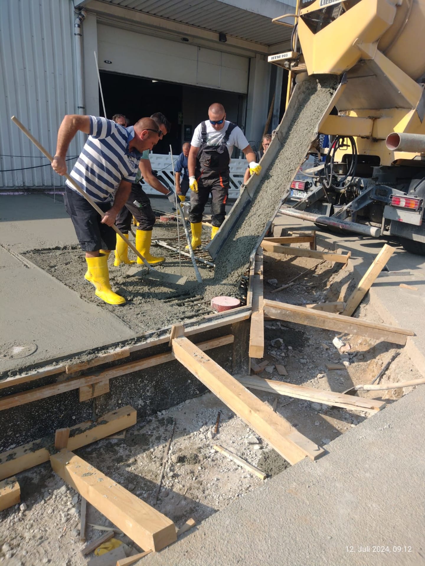 Mitarbeiter verteilen frisch eingebrachten Industriebeton mit der Rüttelbohle