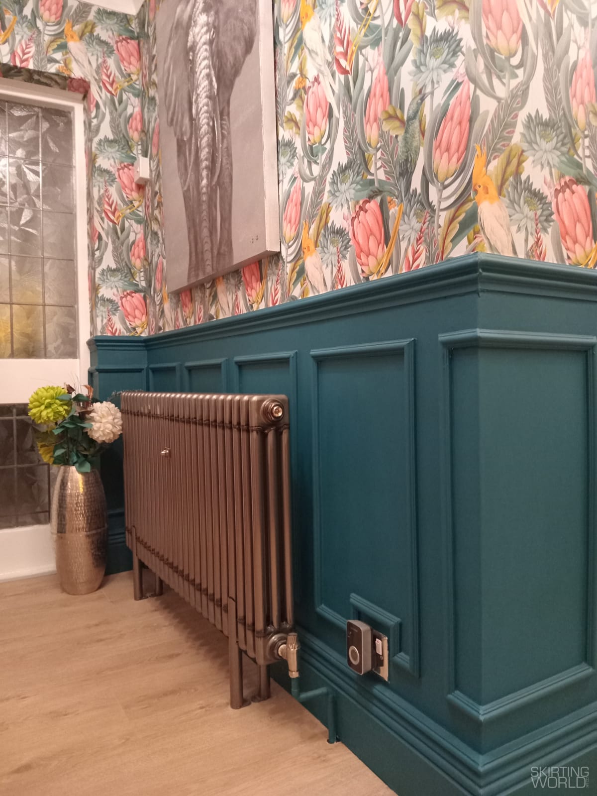 Deep teal skirting and lower wall panelling in a hallway with tropical wallpaper above