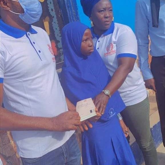 A schoolgirl in a blue hijab receiving an envelope from DRF volunteers