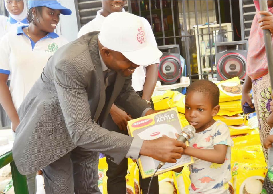 A man in a DRF cap presenting a boxed kettle to a young child