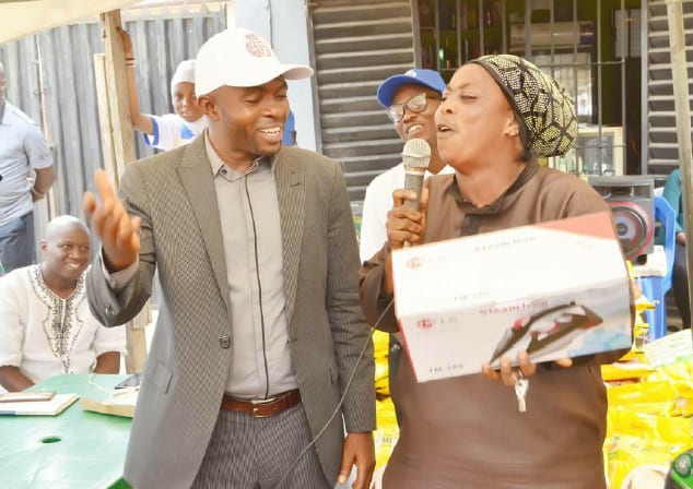 A woman holding a microphone and a boxed pressing iron she received at the food support drive
