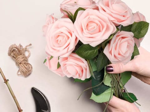 Hands arranging a bouquet of pink artificial real-touch roses