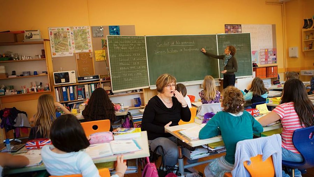 La codeuse assise devant l'élève bénéficiant d'implants cochléaires complète le cours prononcé par l'enseignante. (Amélie Benoist/ BSIP)