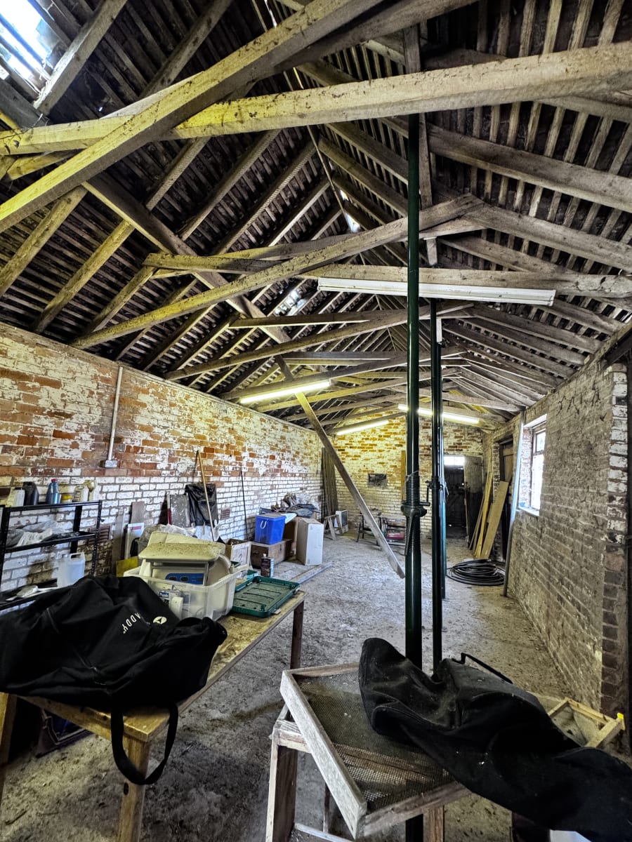 Historic brick barn interior with exposed timber roof trusses, temporary support posts, and construction materials
