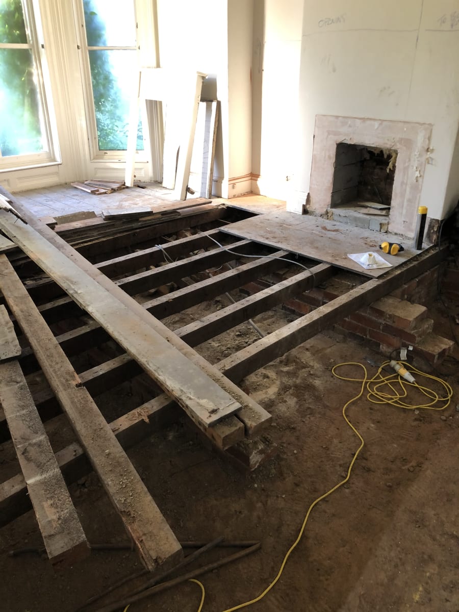Exposed timber floor joists and brick hearth base during renovation, with original fireplace surround exposed above