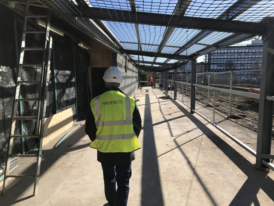 JSA Architects team member in high-vis vest and hard hat walking through covered walkway at active construction site