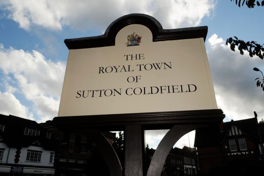 Arched sign reading 'The Royal Town of Sutton Coldfield' with a crest, set against a cloudy sky and town buildings