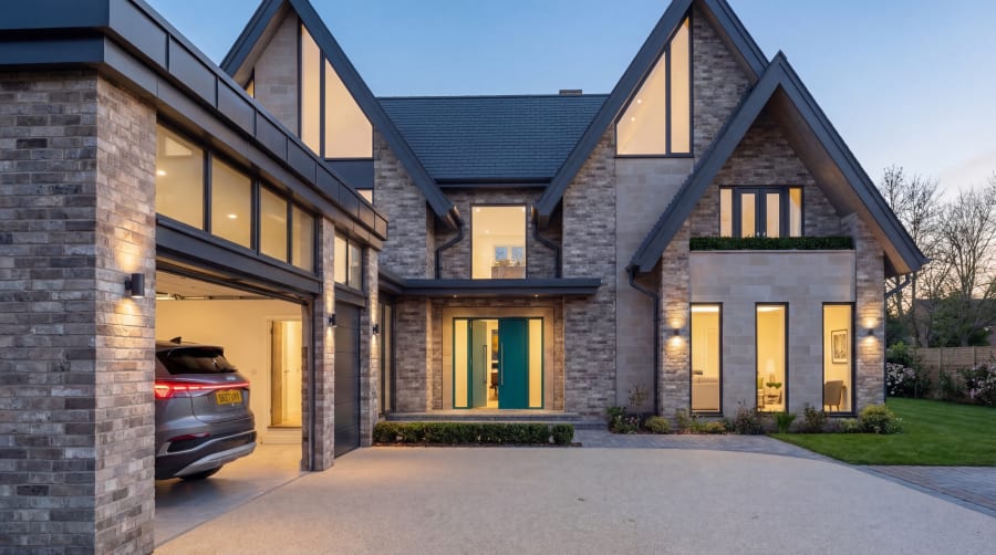 Twilight exterior of a contemporary brick house with steep gables, teal front door, and integral garage