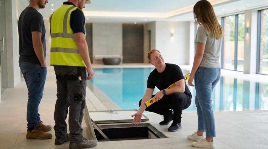 Site team inspects an access hatch in the floor beside an indoor swimming pool during construction