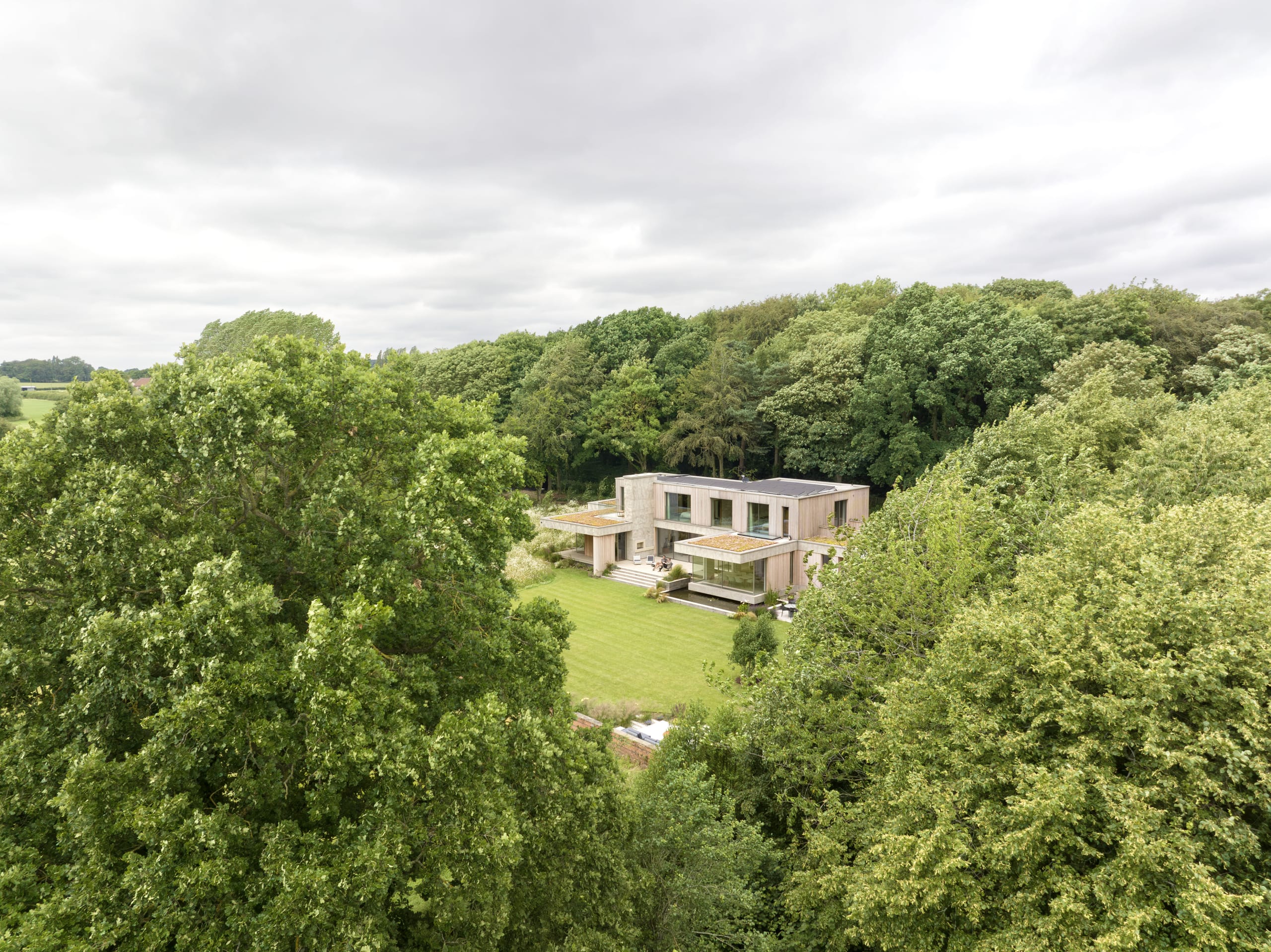 Aerial view of a flat-roofed contemporary house set in a clearing surrounded by dense woodland