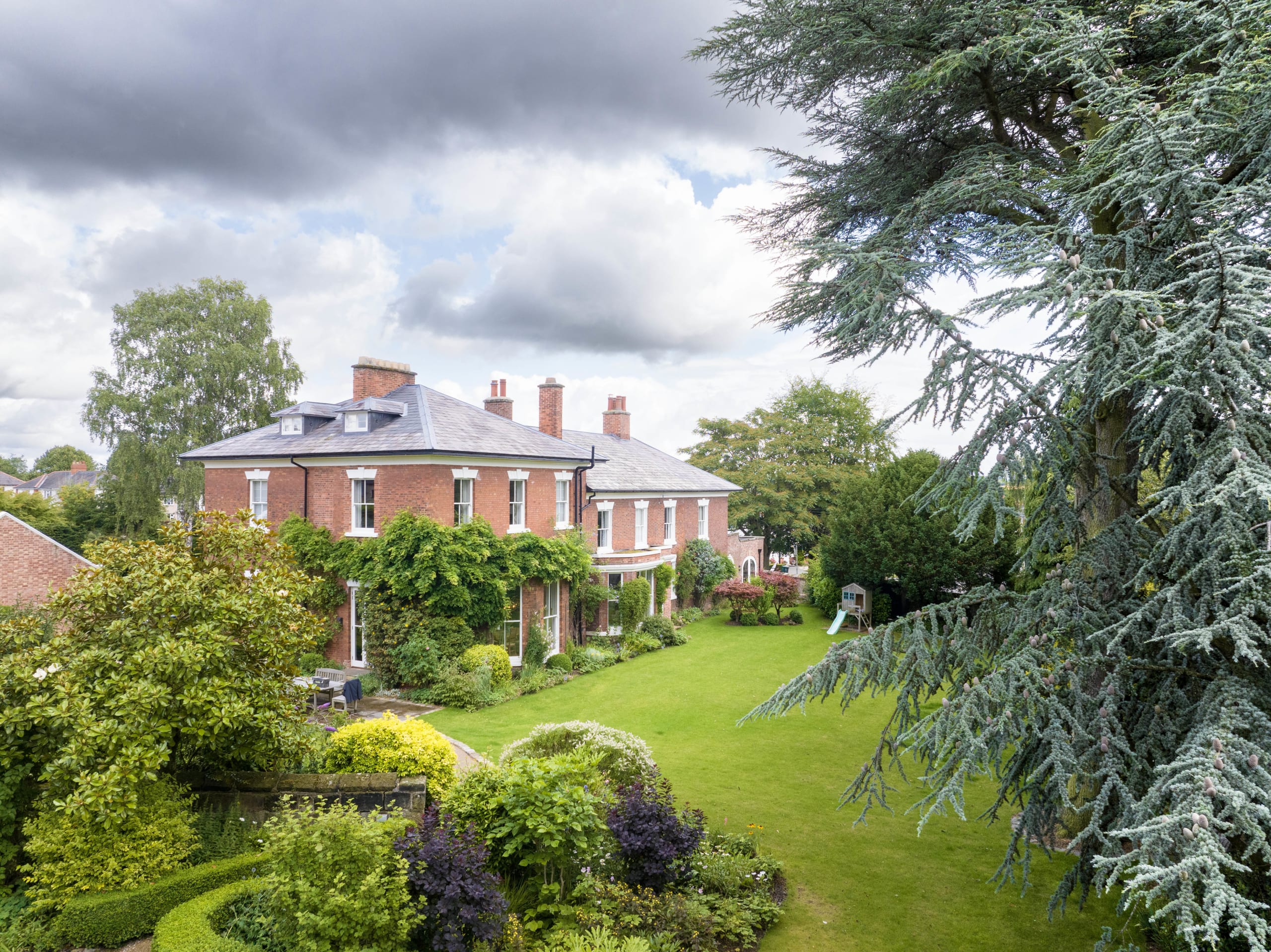 Georgian red brick mansion with slate roof, white-framed windows, curved bay extension, and manicured English garden lawn