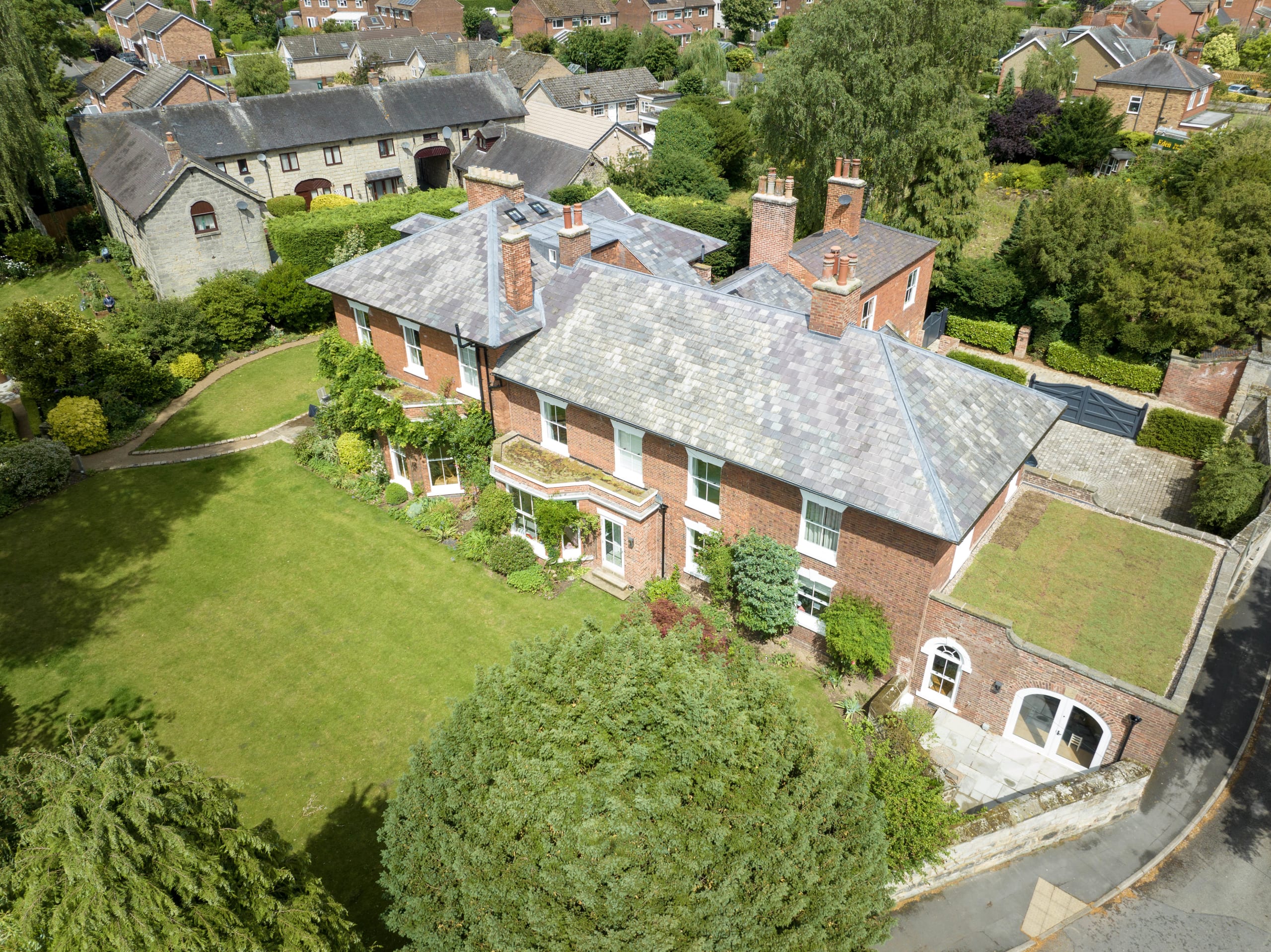 Aerial view of a Georgian red brick manor house with slate roof, bay windows, and manicured lawn gardens