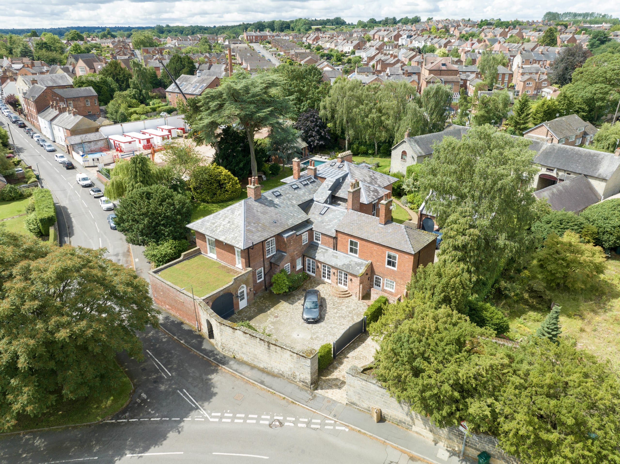 Aerial view of traditional red brick English house with slate roof, landscaped gardens, and cobblestone driveway