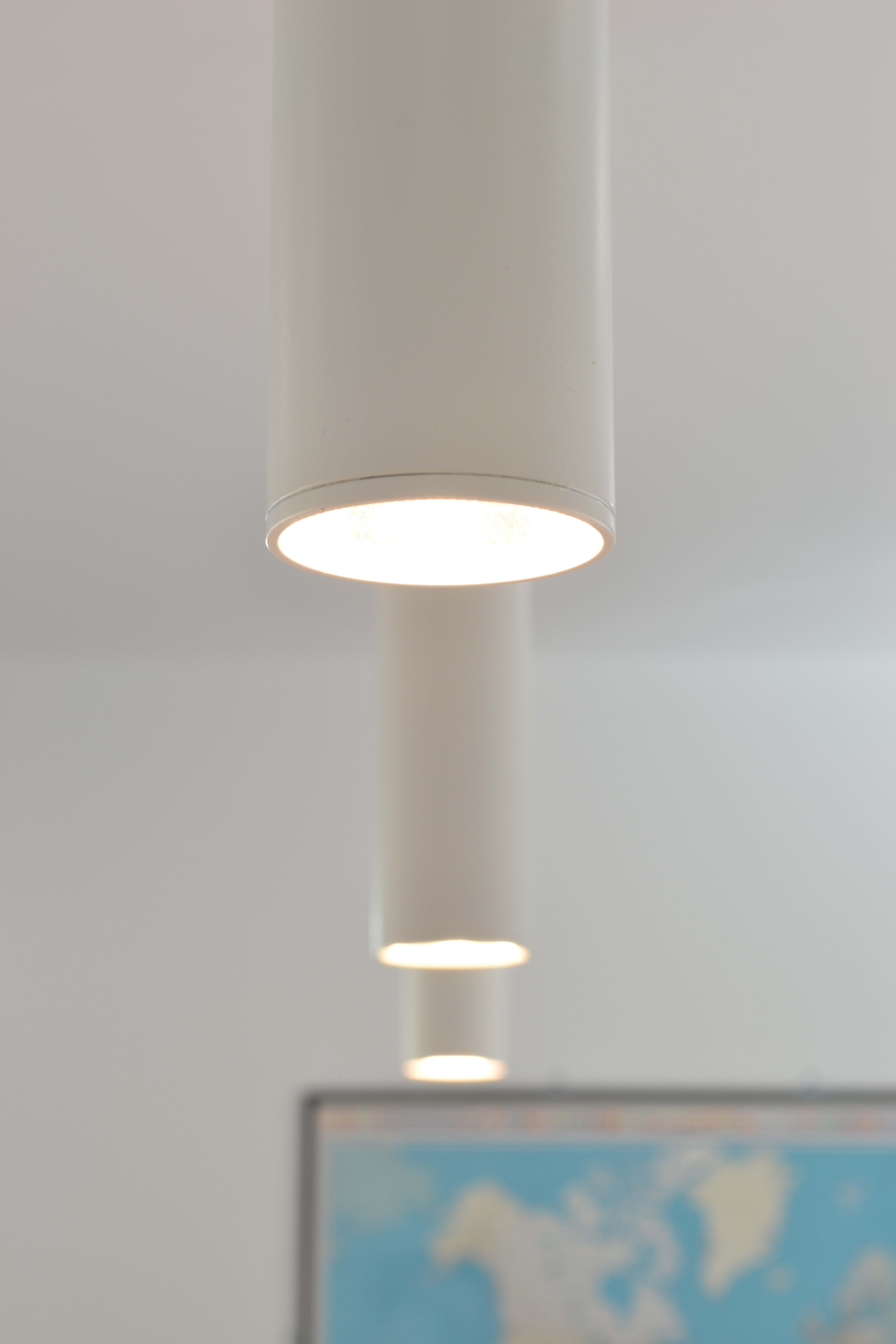 White cylindrical pendant lights with warm LED illumination hanging from ceiling, world map visible in background