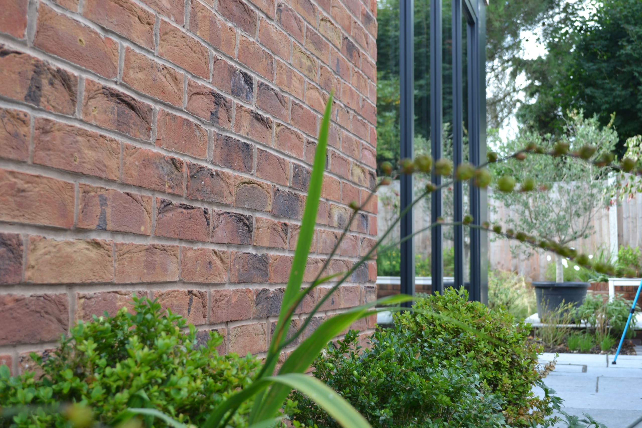 Curved red brick wall detail with landscaped garden featuring boxwood shrubs and ornamental grasses