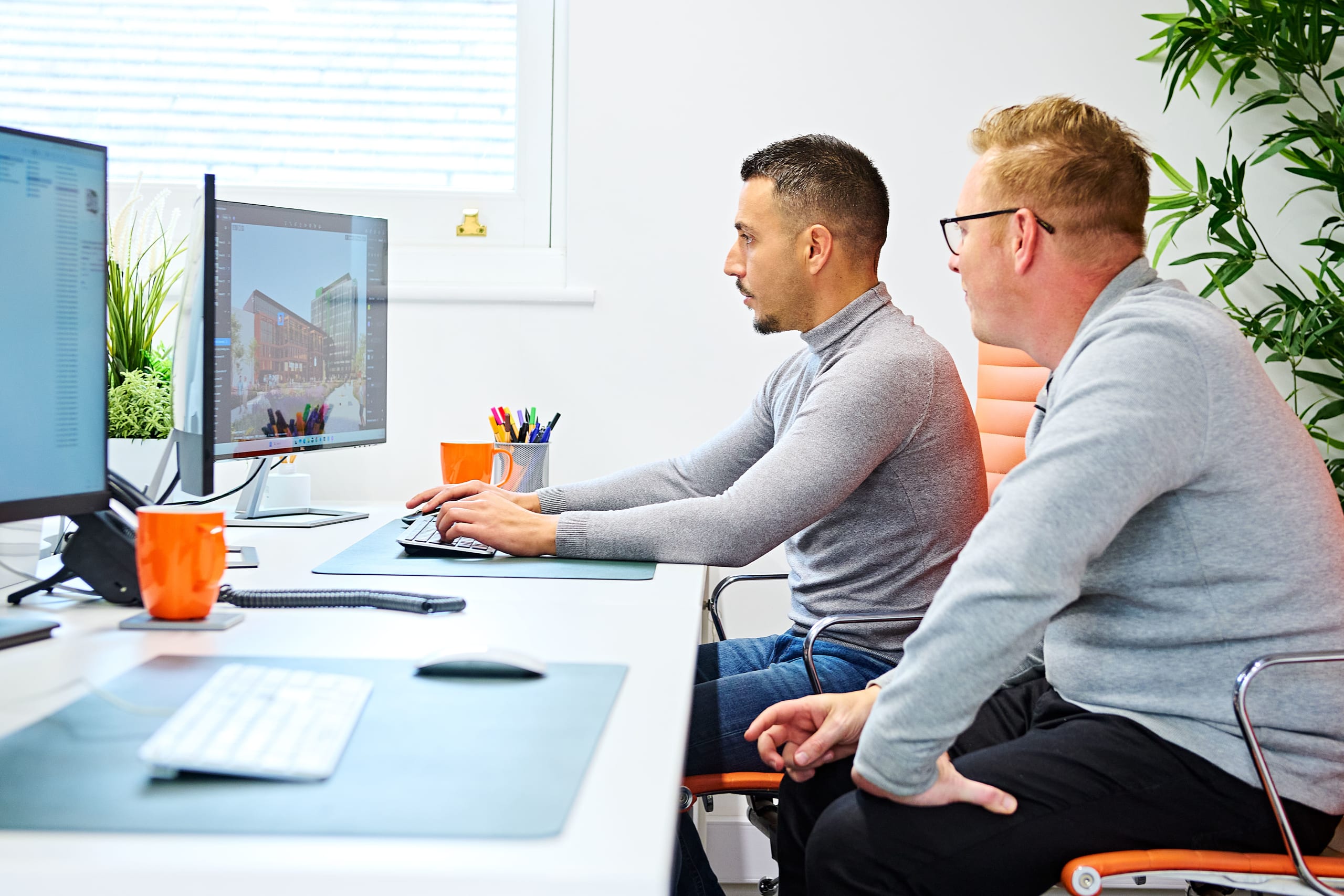 Two architects reviewing a 3D building rendering on computer monitors in a modern office workspace