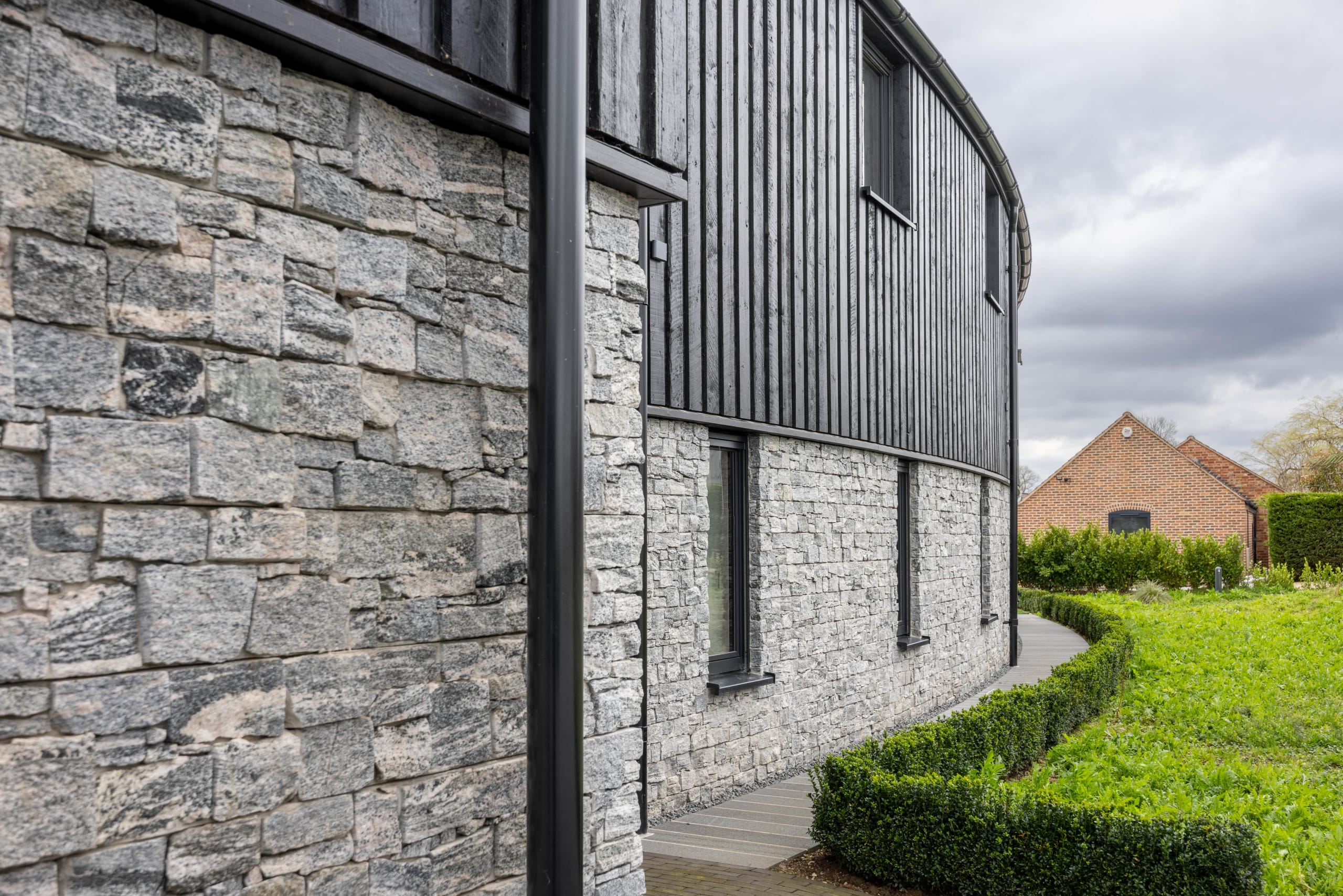 Curved building facade combining coursed stone rubble base with dark vertical timber cladding above