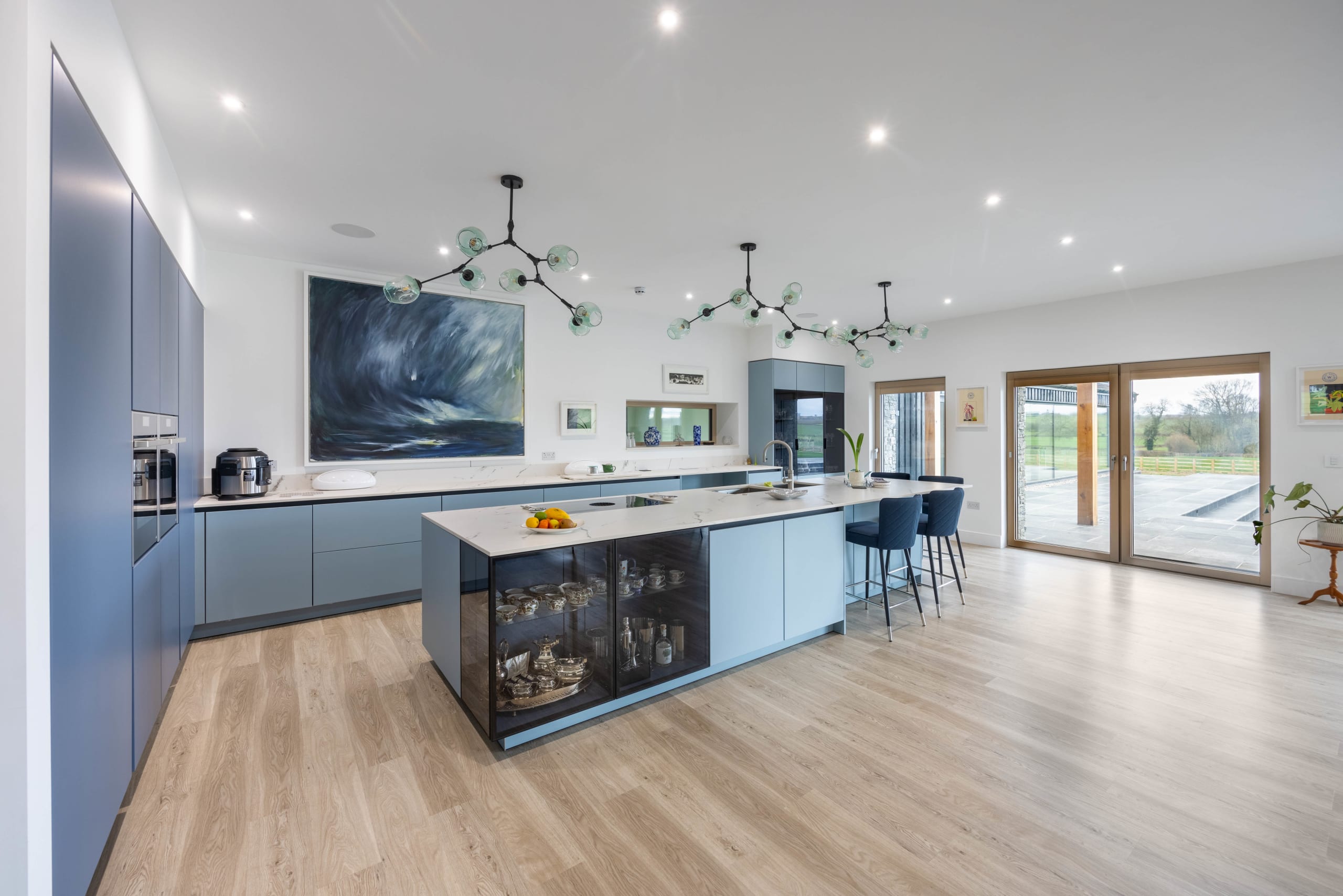 Open-plan kitchen with slate-blue cabinetry, large island, and branching glass-globe pendant lights above light oak flooring