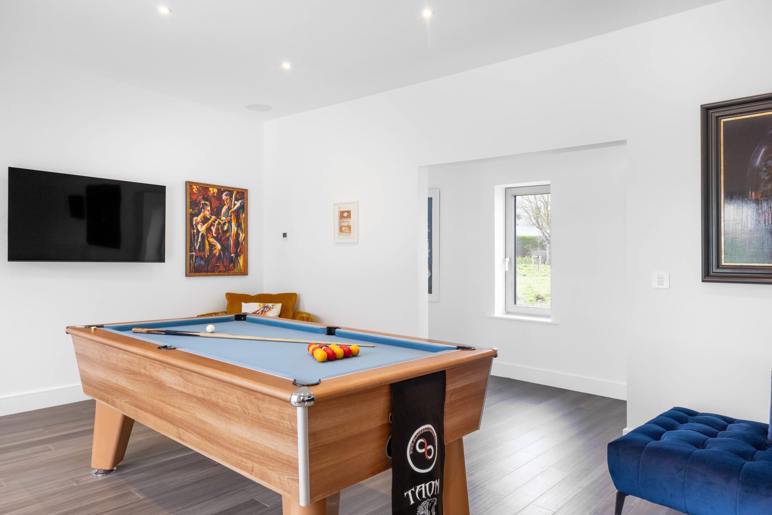 Games room with wooden pool table, blue felt, and wall-mounted TV in a white-walled home extension