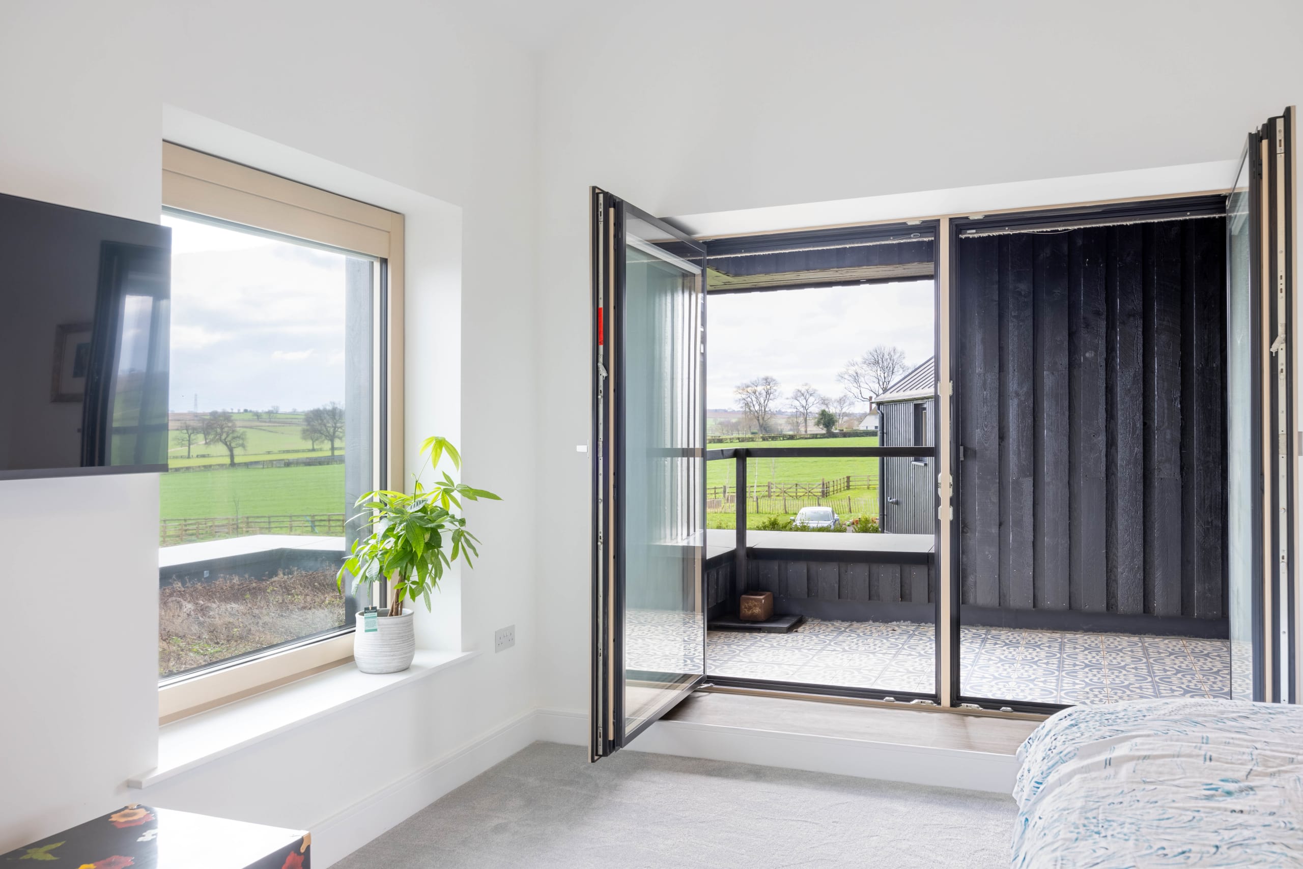 Bedroom with folding glass doors opening to a black timber-clad balcony overlooking farmland