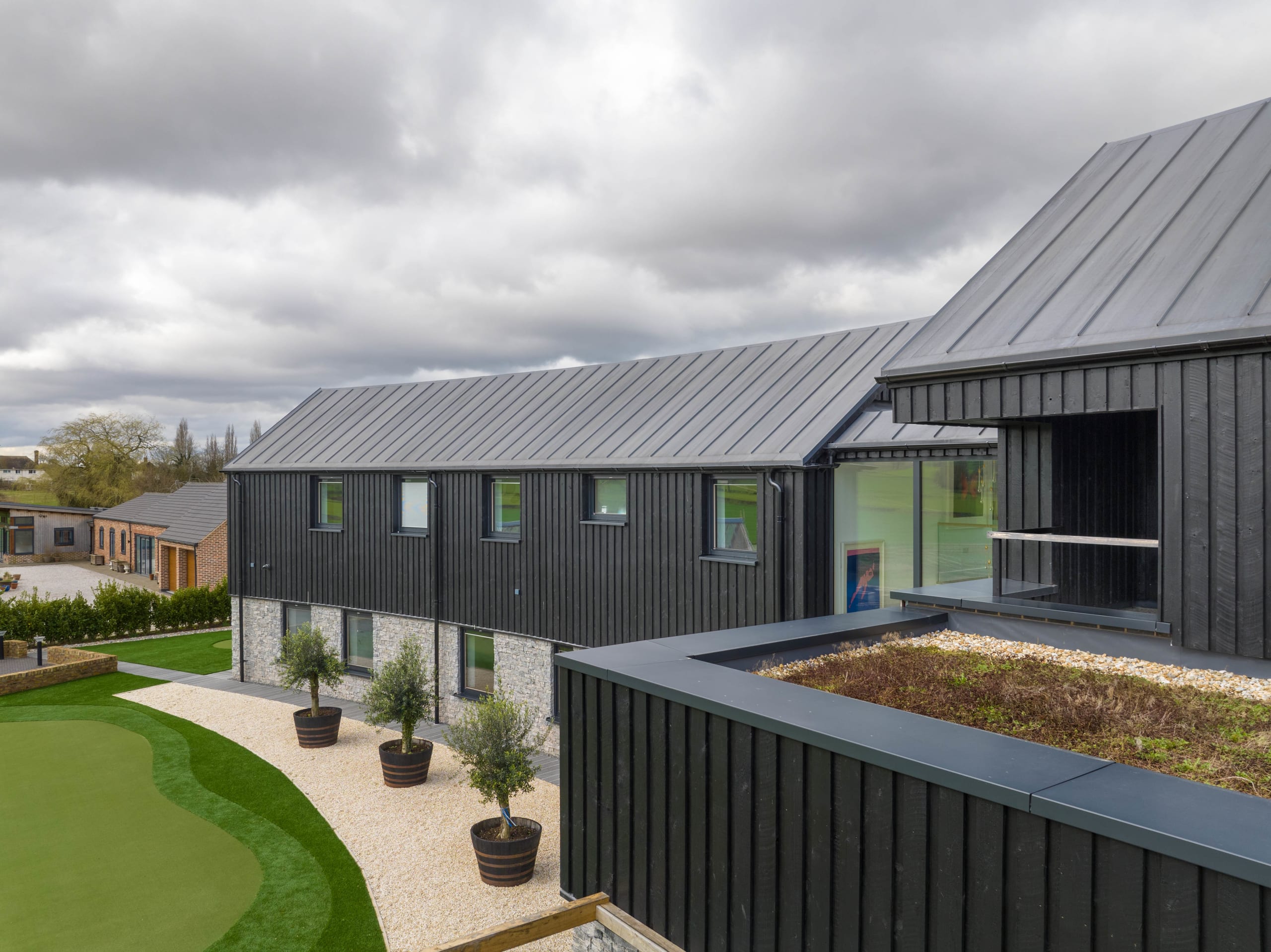 Barn-style house with black timber cladding, standing-seam zinc roof, and a sedum green roof over a garden room