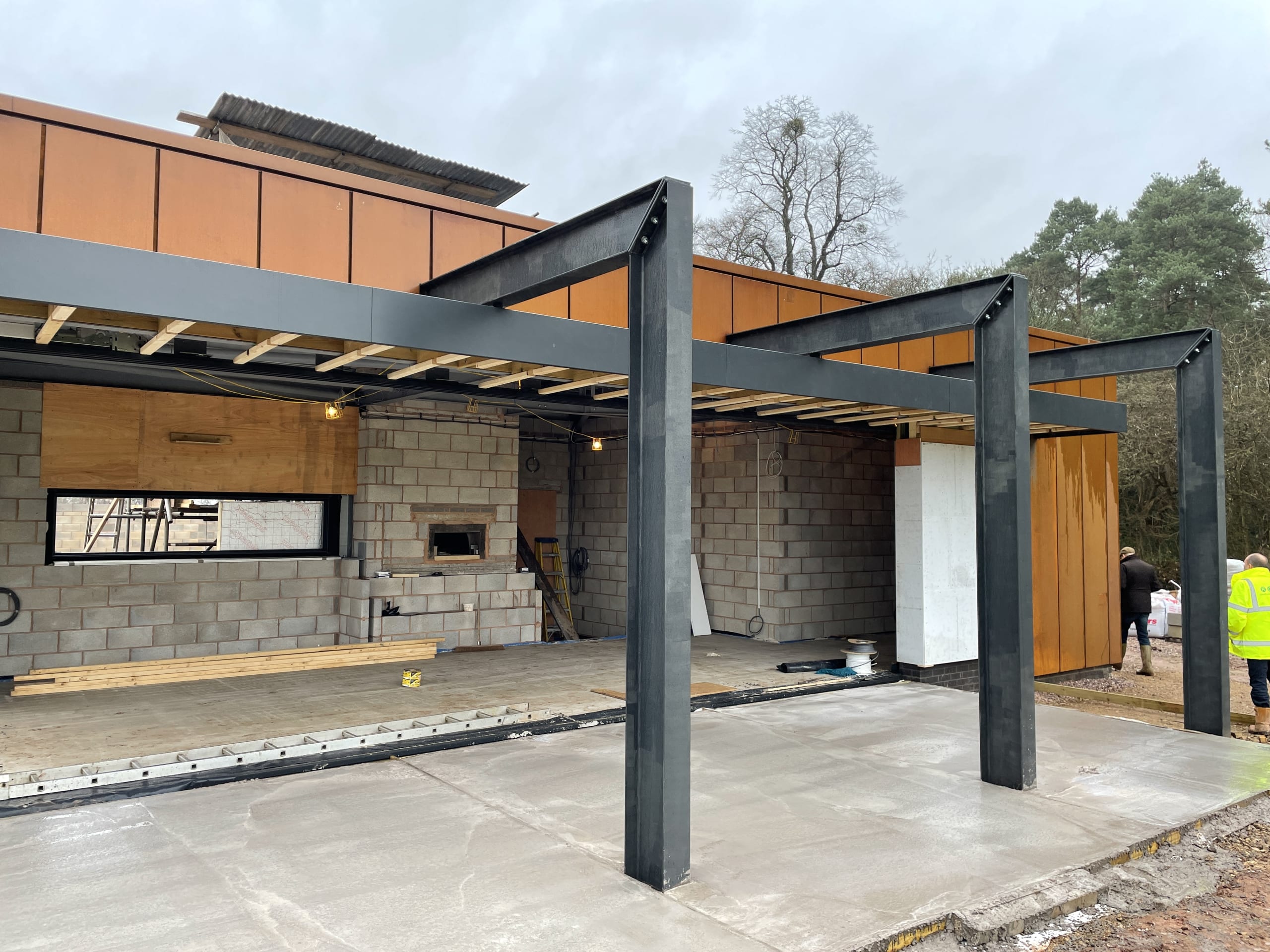 Modern building under construction with steel frame pergola, corten cladding, concrete block walls and fresh concrete patio