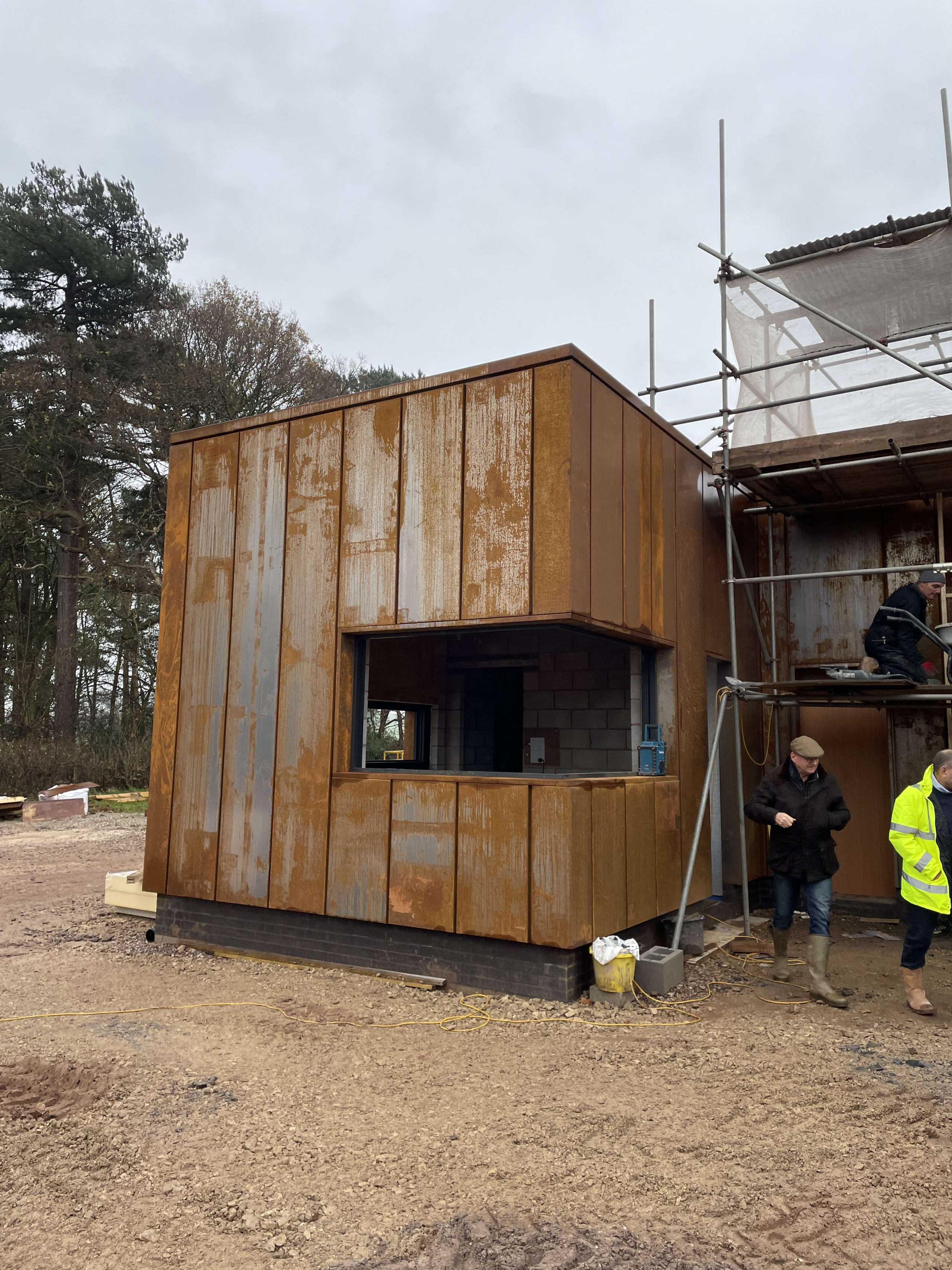 Modern building extension with Corten steel cladding under construction, featuring large window opening and scaffolding