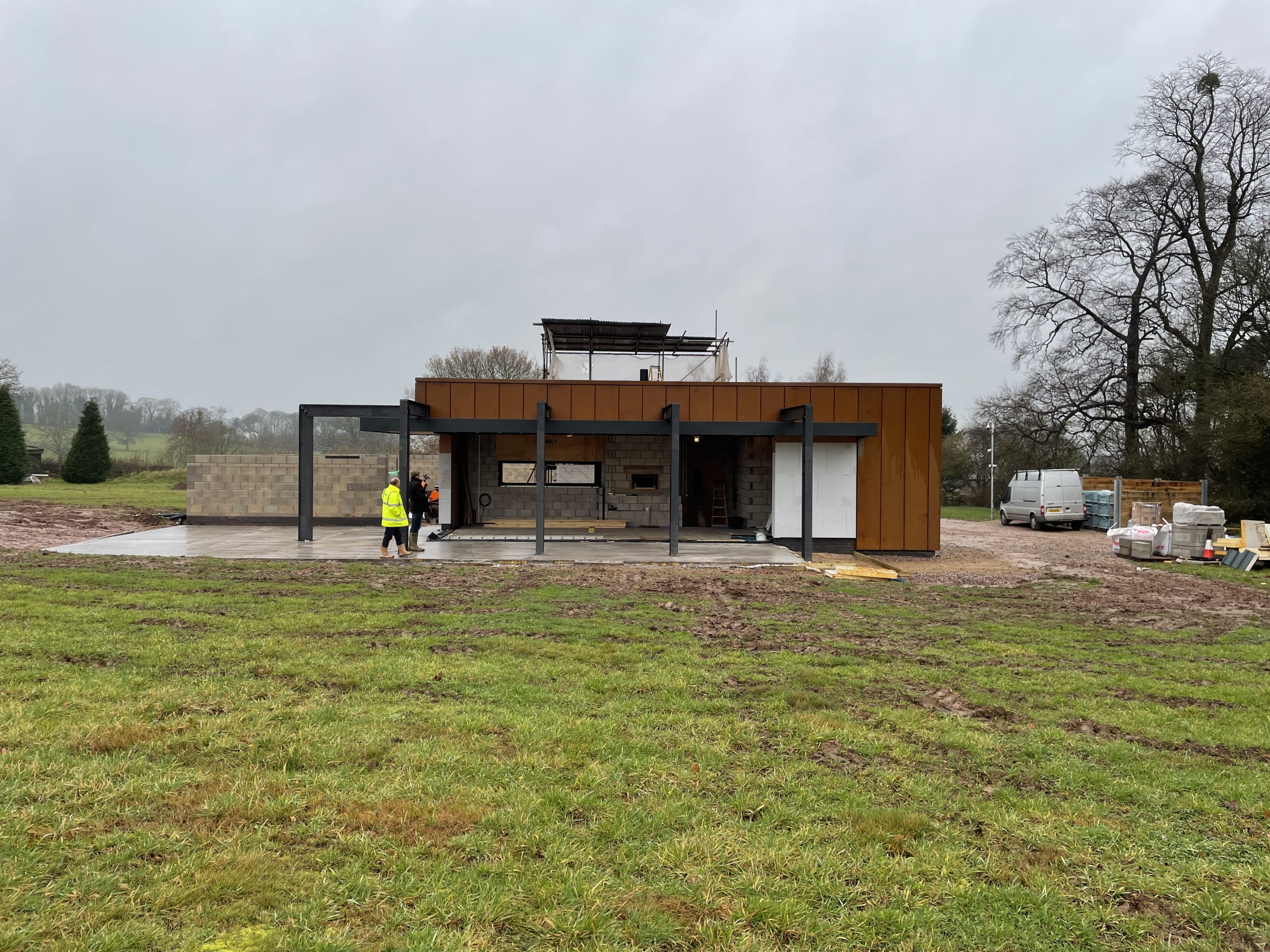 Modern single-story building under construction with corten steel cladding, steel frame, and concrete slab in rural setting