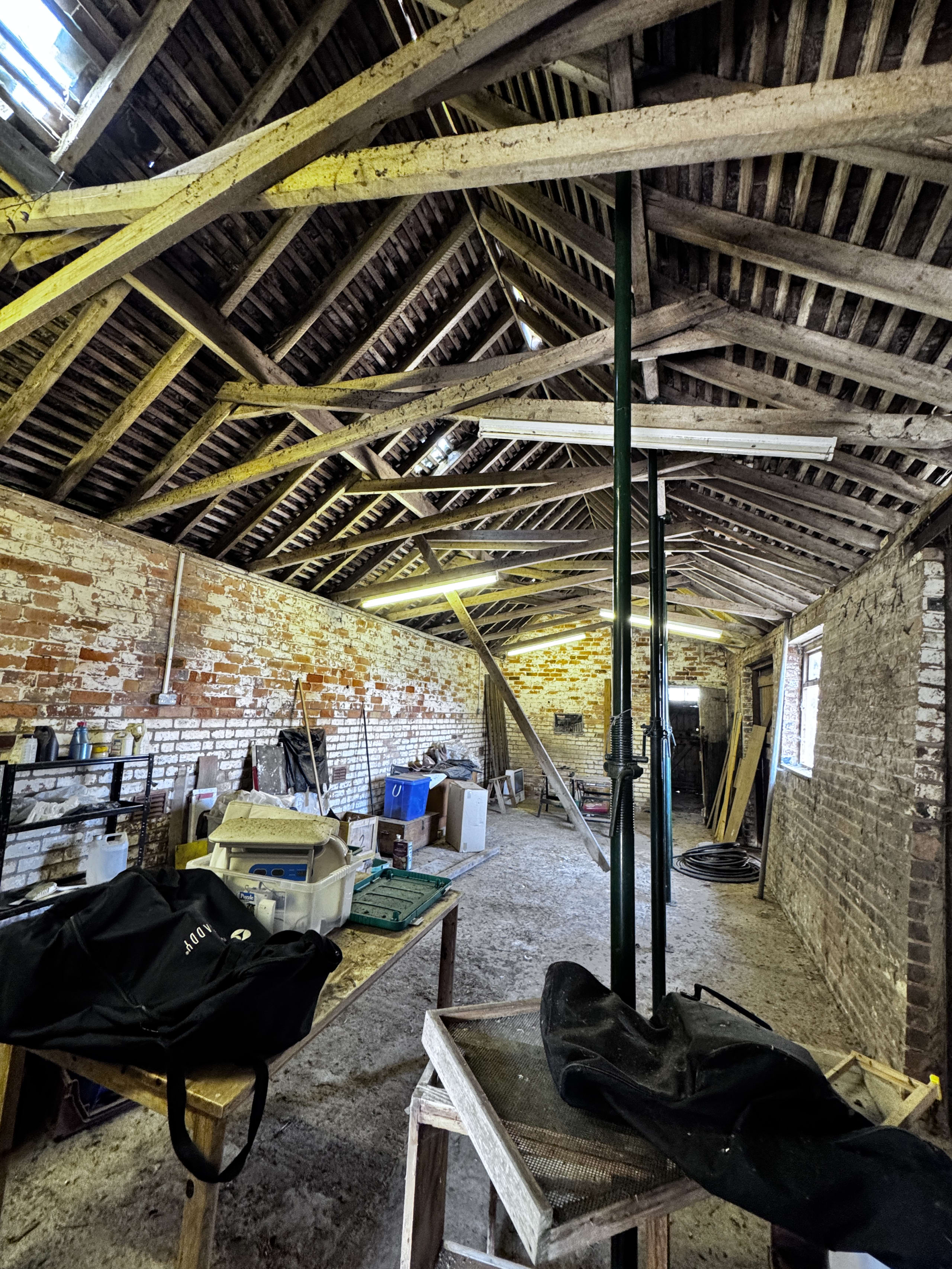 Historic brick barn interior with exposed timber roof trusses, temporary support posts, and construction materials